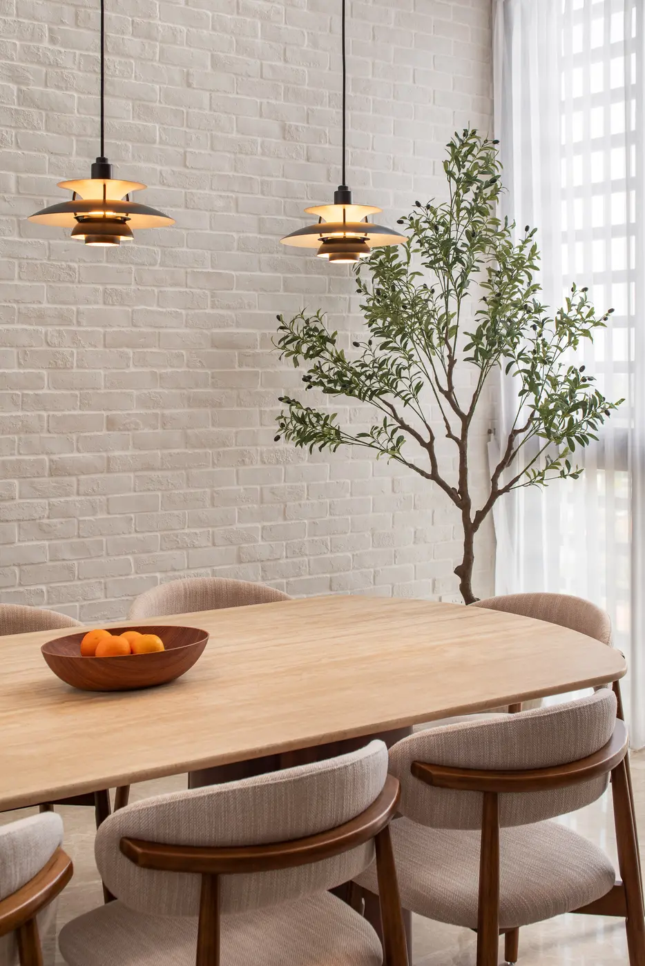 Dining table close-up — PH pendants glowing above travertine surface and olive tree