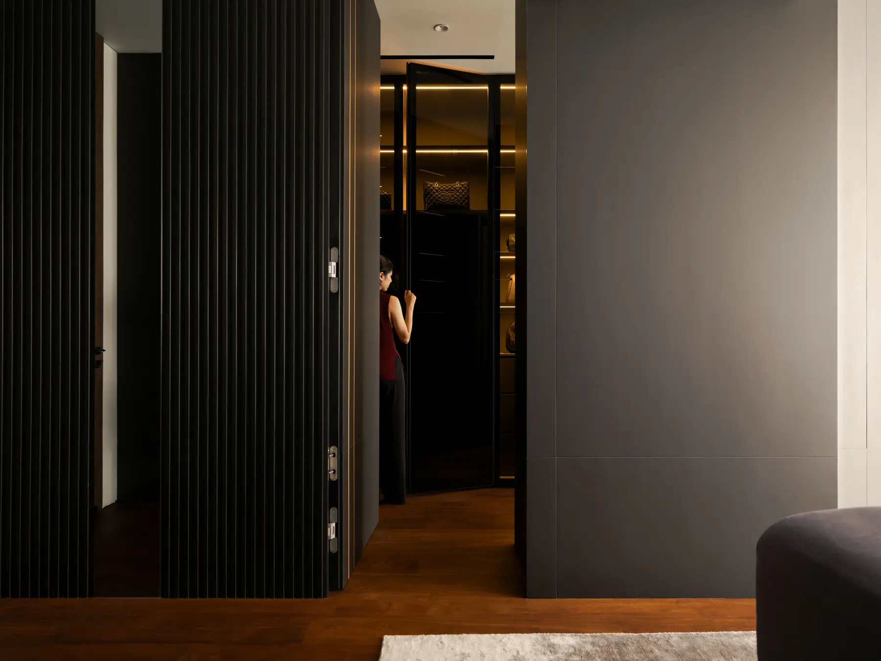 Concealed pivot door — dark panelling revealing a walk-in wardrobe with lit shelving beyond