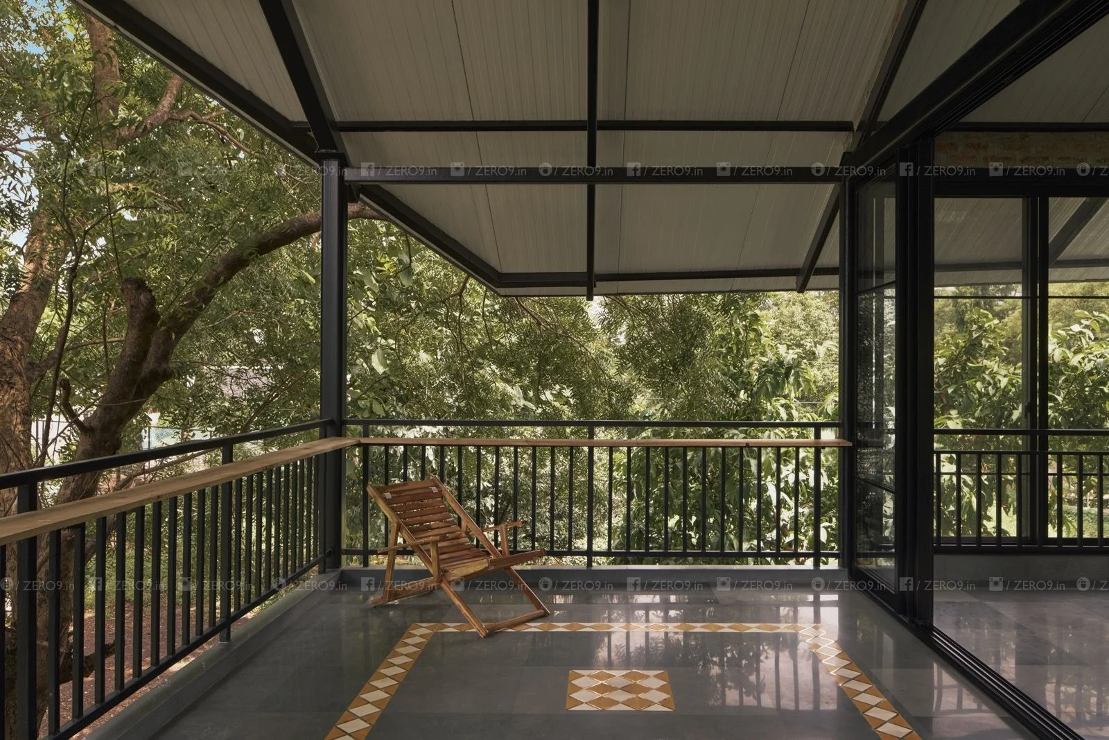 The first-floor balcony extends into the treetops, with a peripheral timber ledge and patterned floor tile, a wooden chair overlooking the canopy