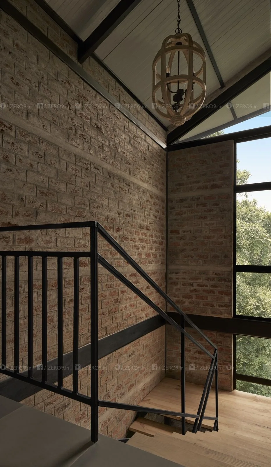 Interior staircase — steel railing, exposed brickwork, triangular roof glazing and a pendant light suspended from the steel truss