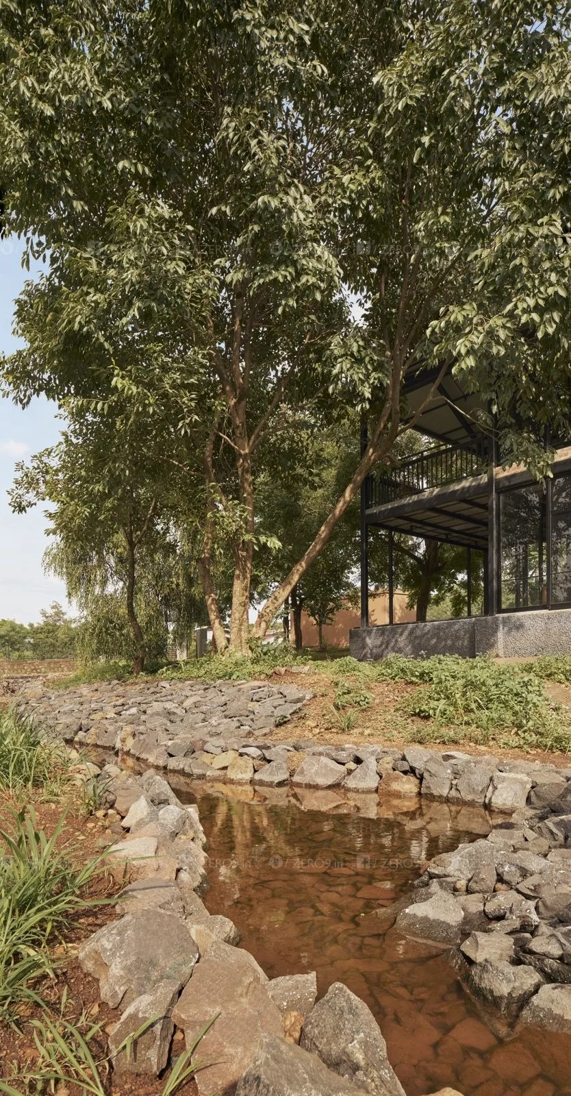 The monsoon stream slowed by stone barriers, forming an aquatic garden beside the house